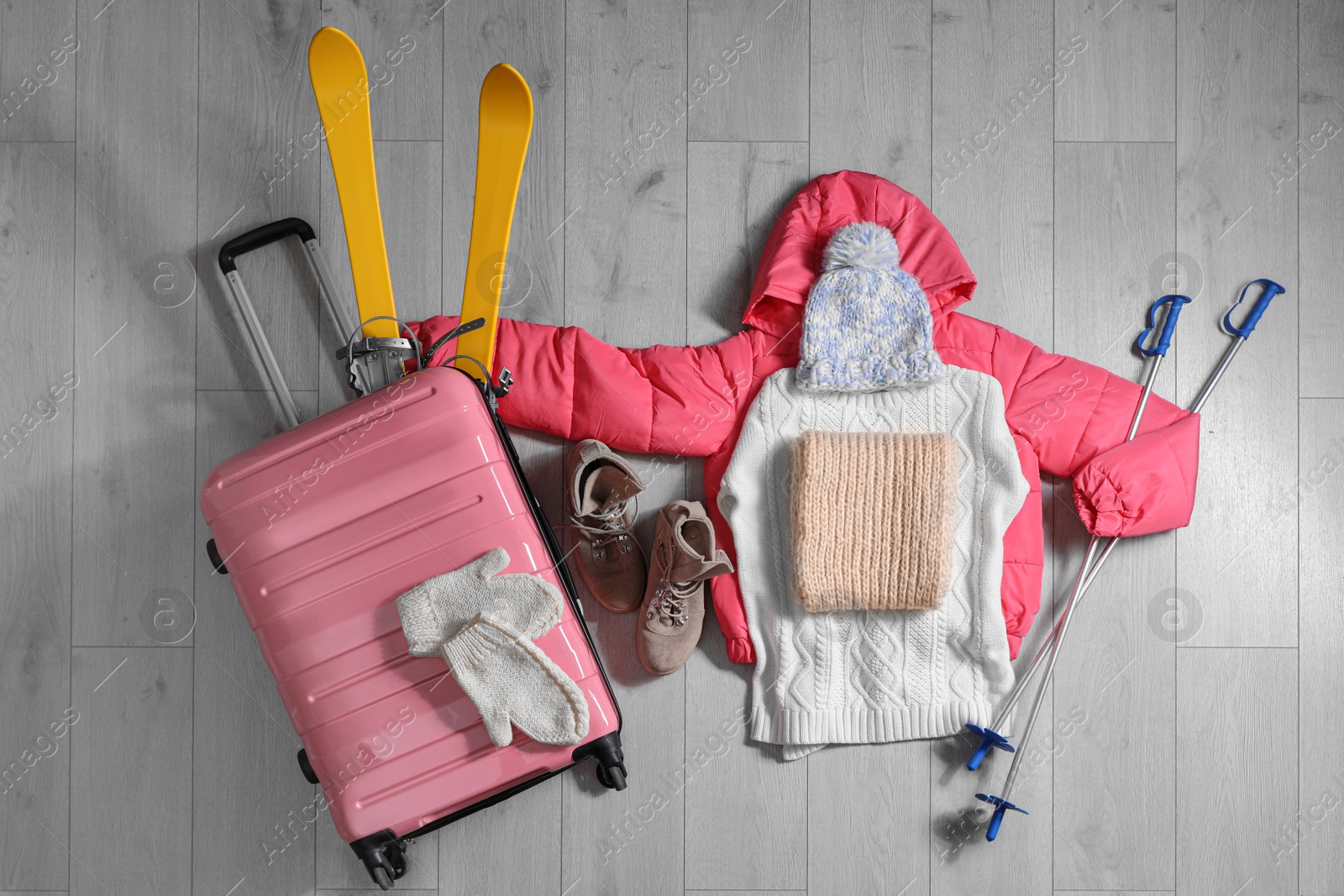 Photo of Suitcase with warm clothes and skis on wooden floor, flat lay. Winter vacation