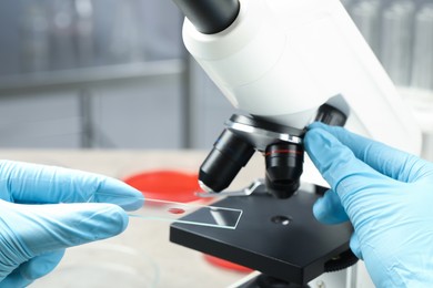 Scientist examining sample of red liquid on slide under microscope in laboratory, closeup