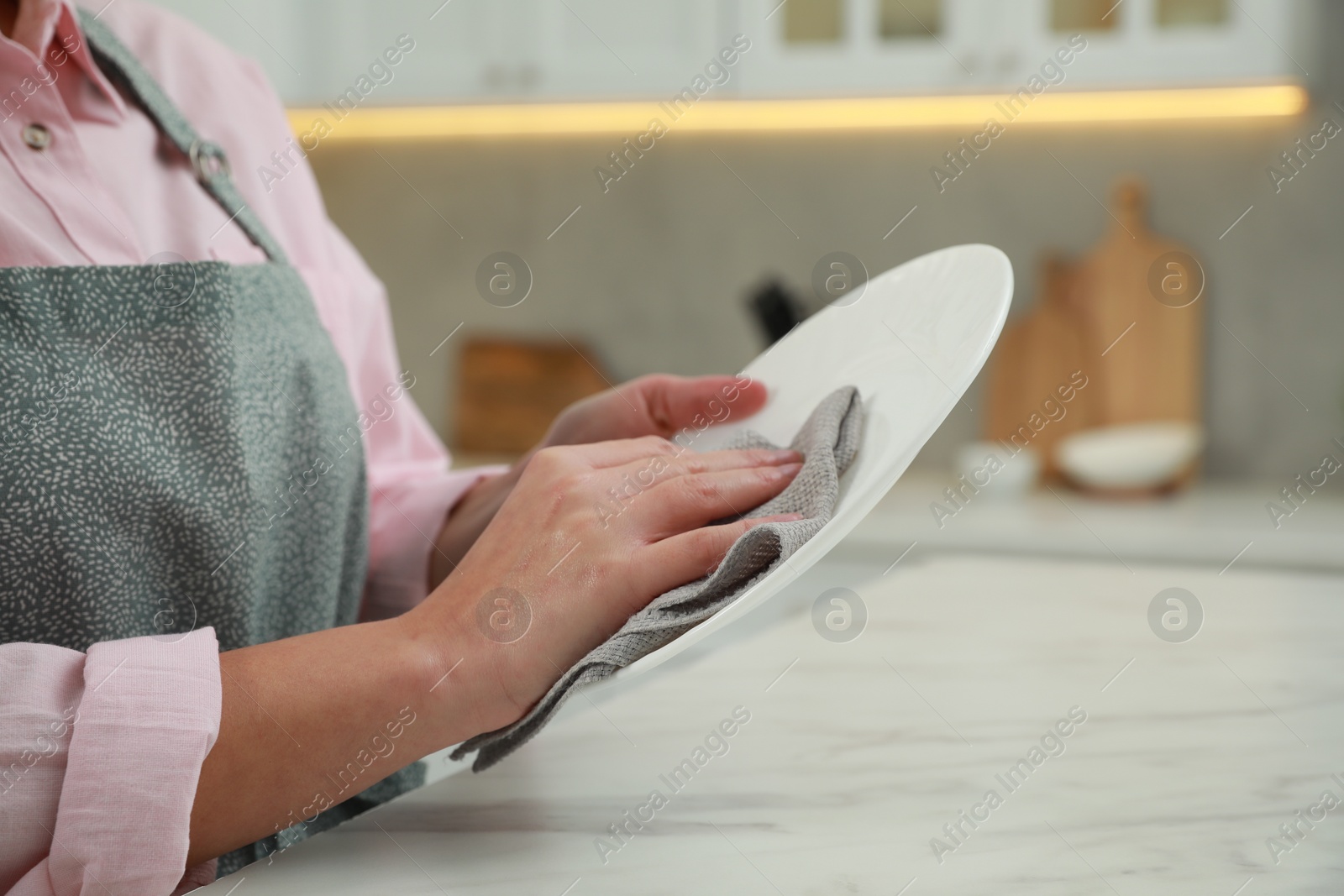Photo of Woman wiping plate with towel at white marble table in kitchen, closeup. Space for text