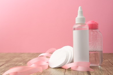 Photo of Composition with makeup removers and cotton pads on wooden table against pink background, space for text