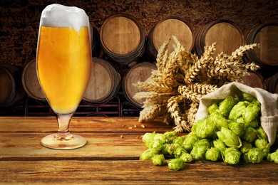 Image of Glass of tasty light beer, fresh hops and wheat spikes on wooden table in cellar
