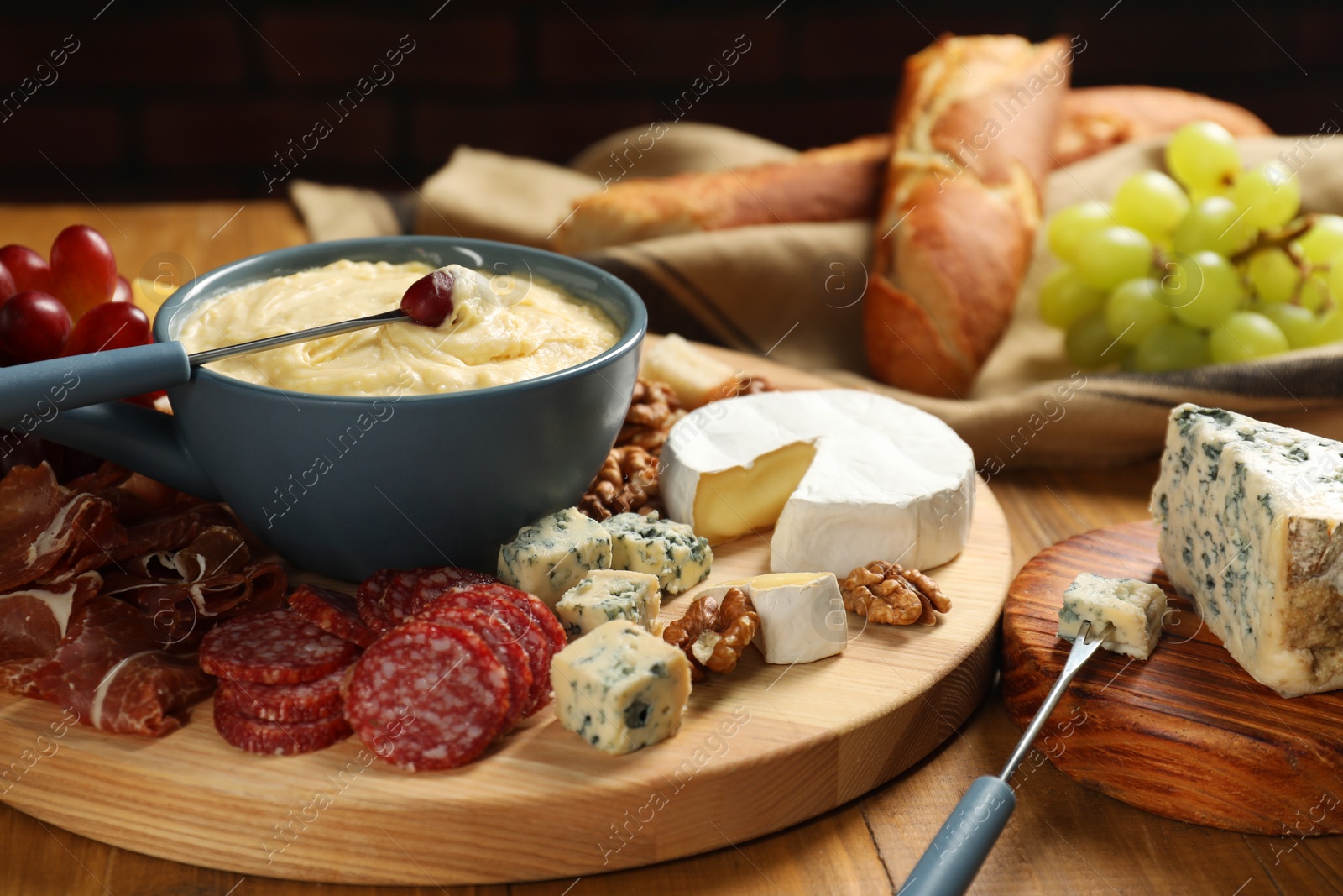 Photo of Fondue pot with tasty melted cheese, forks and different snacks on wooden table