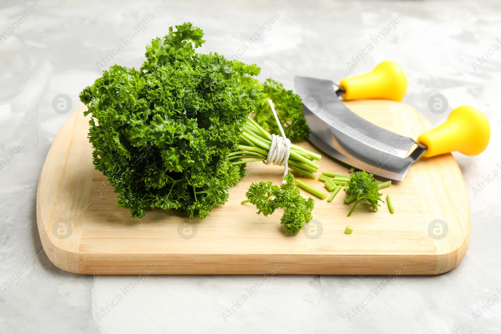 Photo of Fresh curly parsley, cutting board and mincing knife on grey table