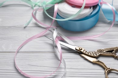 Pair of scissors with colorful ribbons on white wooden table, closeup