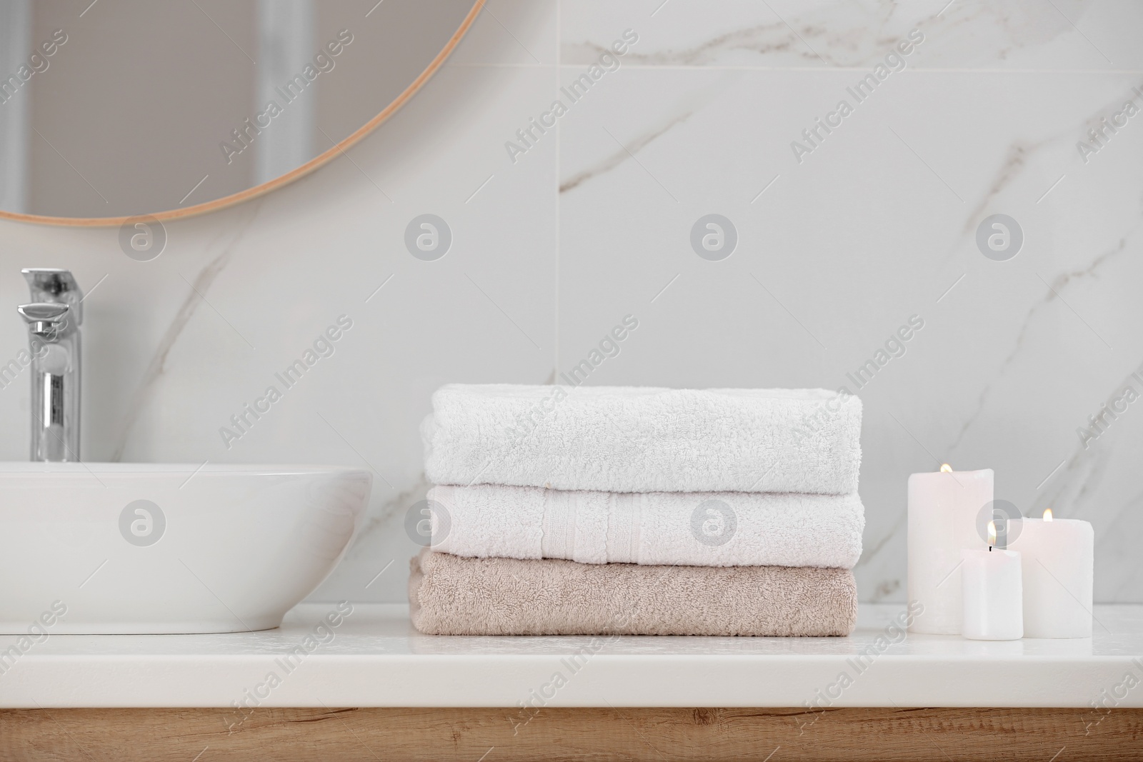 Photo of Clean towels and burning candles on counter in bathroom