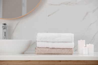 Photo of Clean towels and burning candles on counter in bathroom