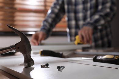 Photo of Man assembling furniture at table indoors, focus on hammer and metal fasteners