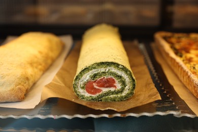 Photo of Delicious sponge roll with salmon and spinach on counter in bakery shop, closeup