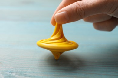 Photo of Woman playing with yellow spinning top at light blue wooden table, closeup