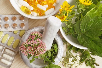 Photo of Mortar with fresh herbs and pills on wooden table, flat lay