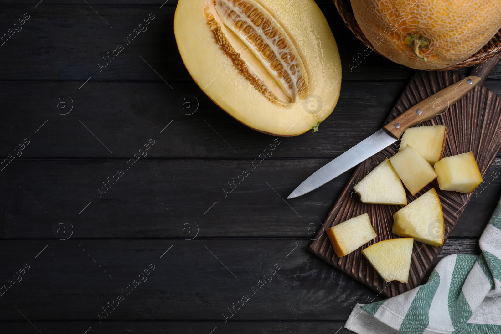 Photo of Pieces of delicious honey melon on black wooden table, flat lay. Space for text