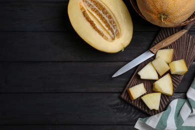 Pieces of delicious honey melon on black wooden table, flat lay. Space for text