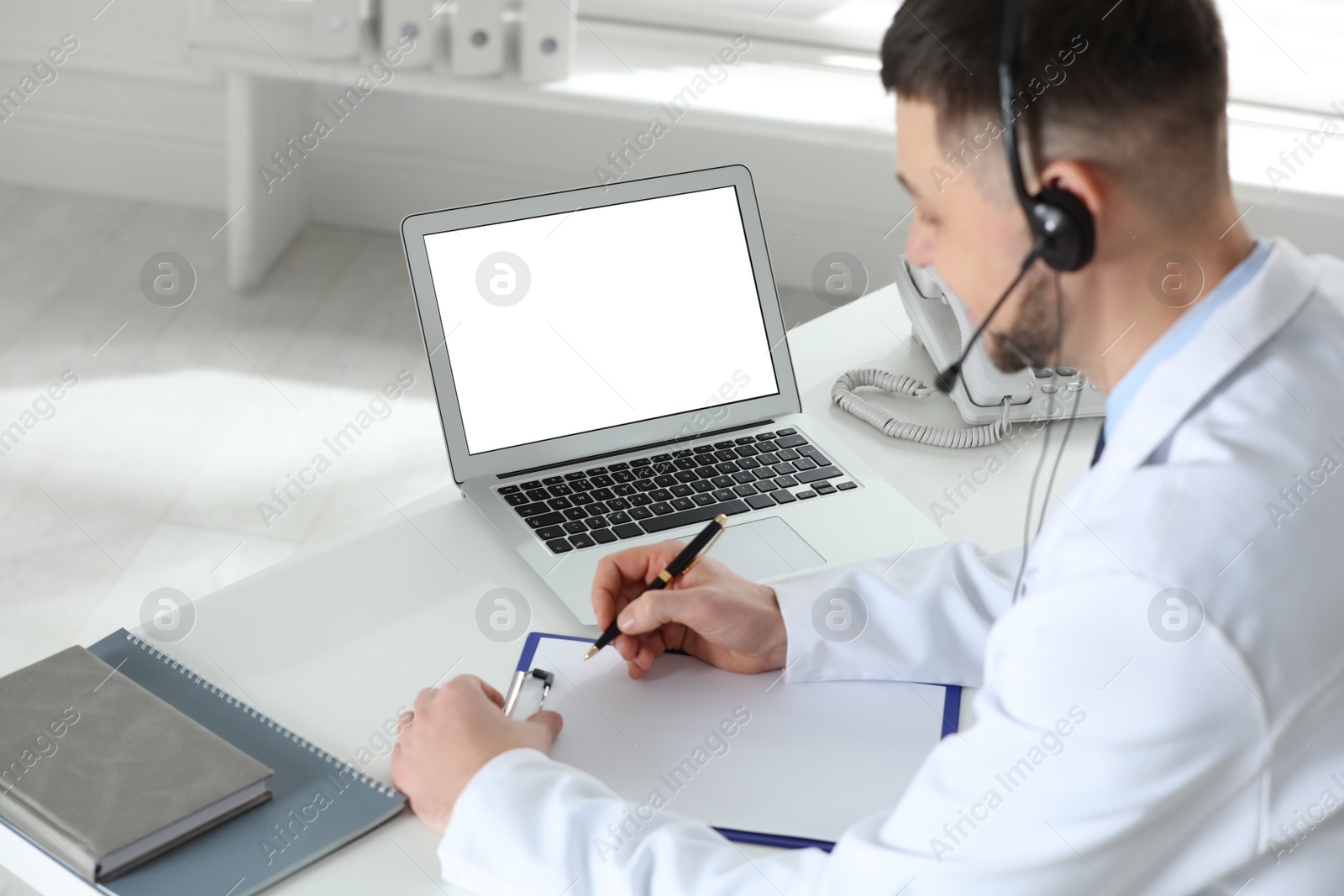 Photo of Doctor with headset consulting patient online at desk in clinic, space for text. Health service hotline