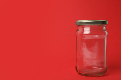 Photo of Closed empty glass jar on red background, space for text