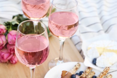 Photo of Glasses of delicious rose wine, flowers and food on white picnic blanket, closeup