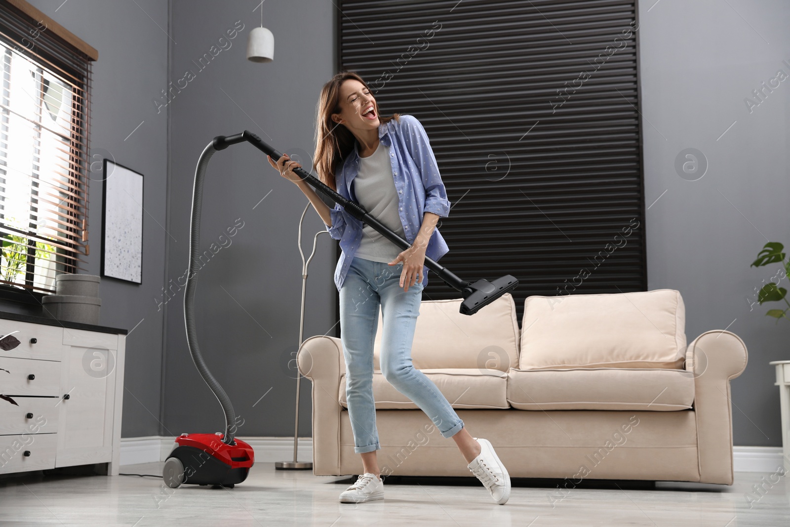 Photo of Young woman having fun while vacuuming at home