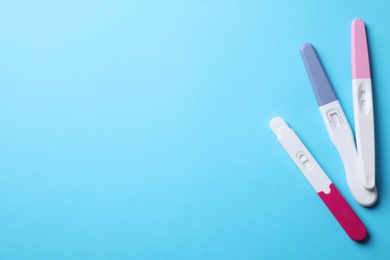 Different pregnancy tests on light blue background, flat lay. Space for text