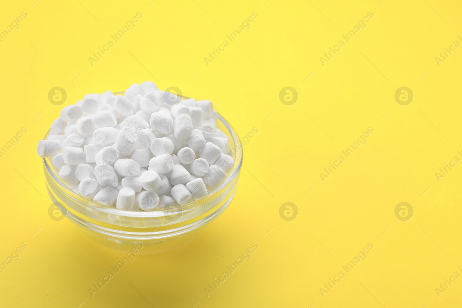 Photo of Glass bowl with delicious marshmallows on yellow background, space for text