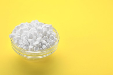 Photo of Glass bowl with delicious marshmallows on yellow background, space for text