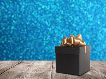 Image of Beautiful gift box on wooden table against shiny light blue background, bokeh effect. Space for text