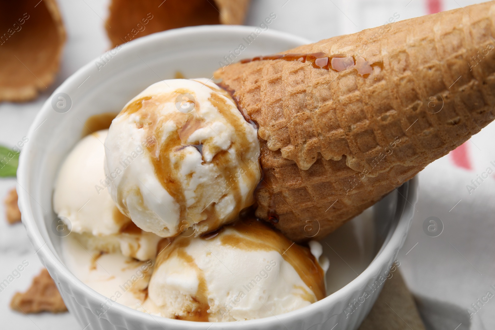 Photo of Scoops of ice cream with caramel sauce and wafer cone in bowl, closeup