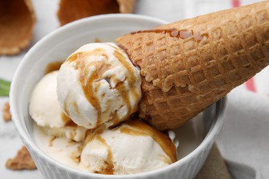 Photo of Scoopsice cream with caramel sauce and wafer cone in bowl, closeup