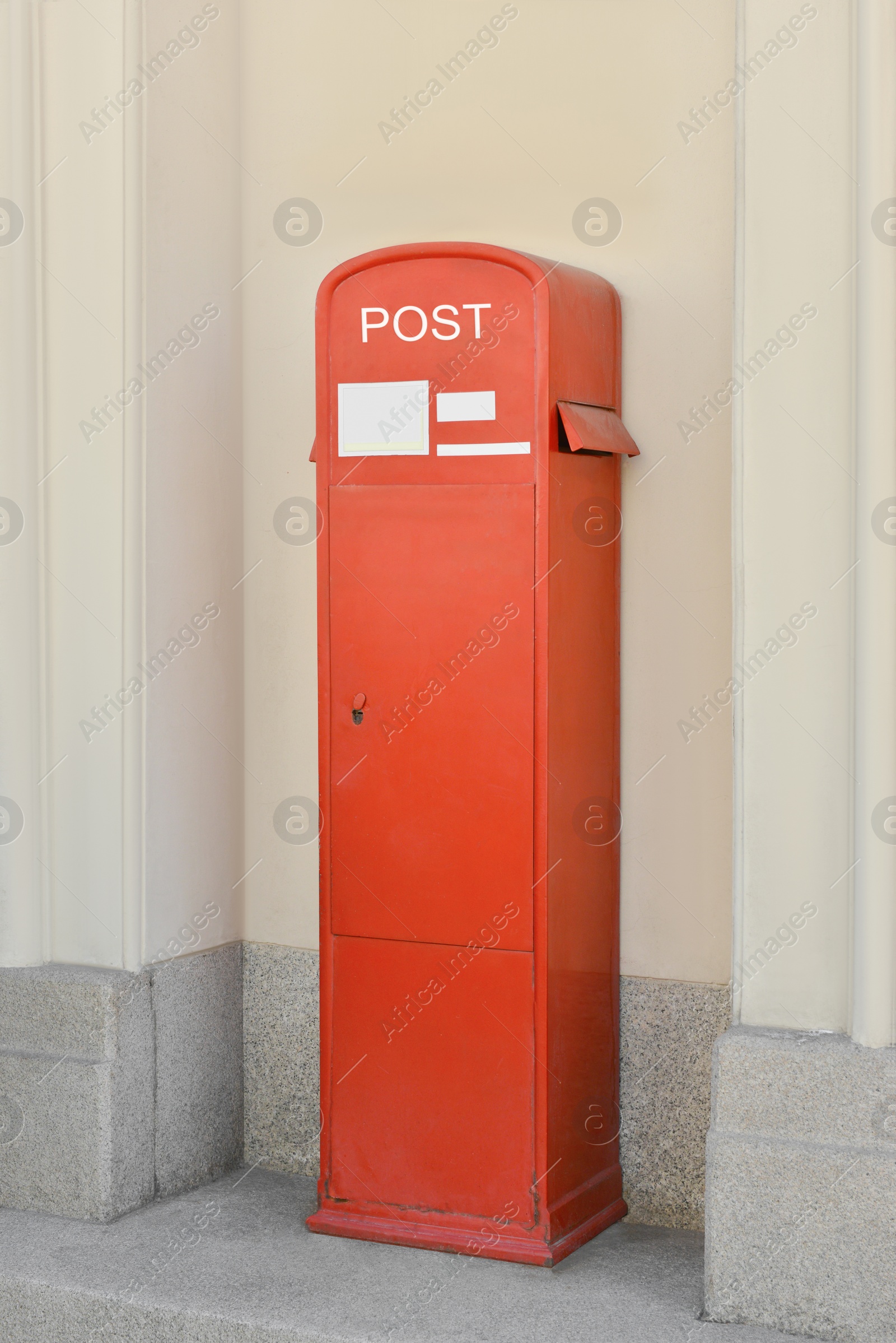 Photo of Red postbox near beige building on summer day