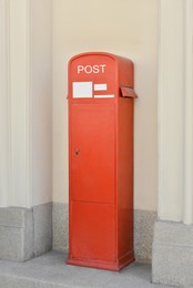 Red postbox near beige building on summer day