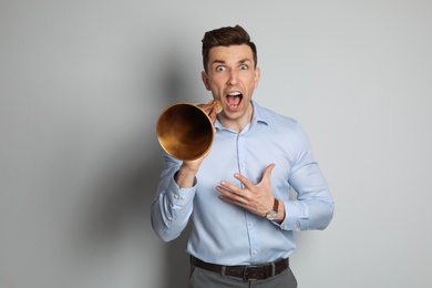 Young man shouting into megaphone on light background