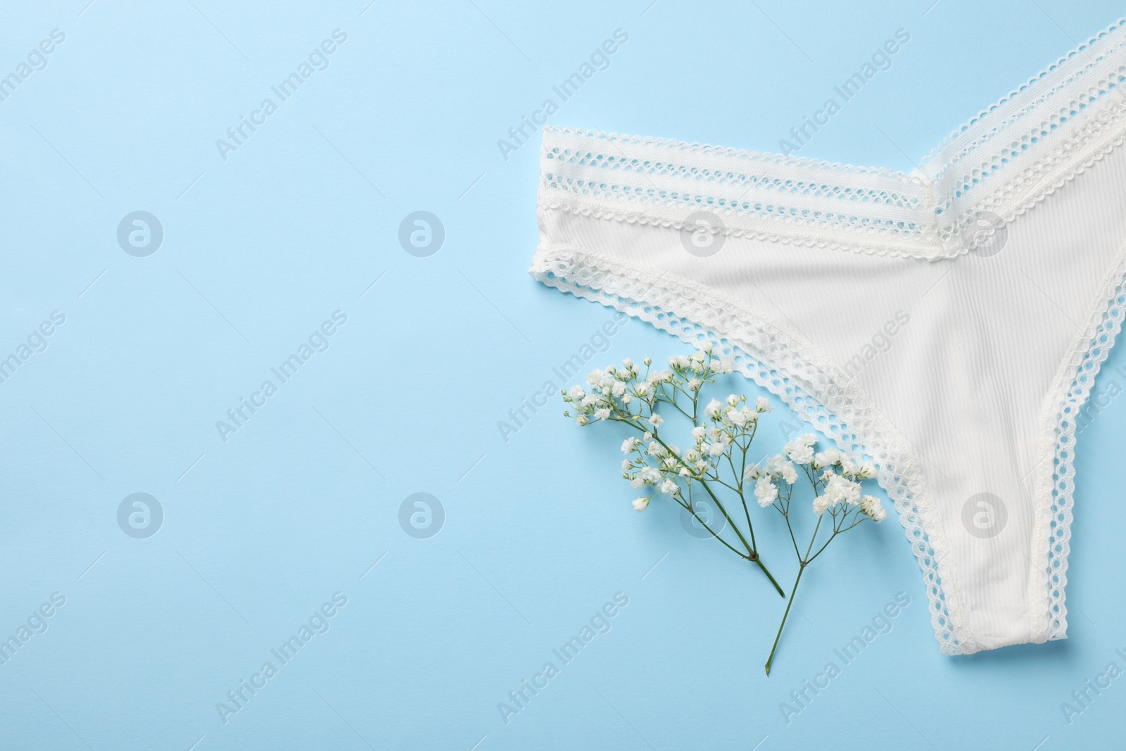Photo of White women's underwear and flowers on light blue background, flat lay. Space for text