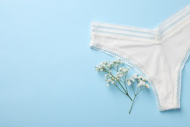 White women's underwear and flowers on light blue background, flat lay. Space for text