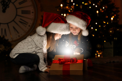 Photo of Cute children opening magic gift box near Christmas tree at night