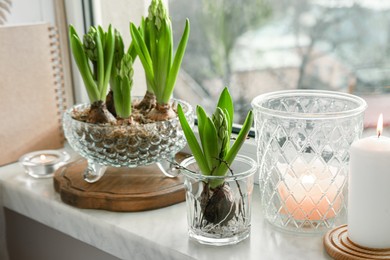 Beautiful bulbous plants and burning candles on windowsill indoors. Spring time