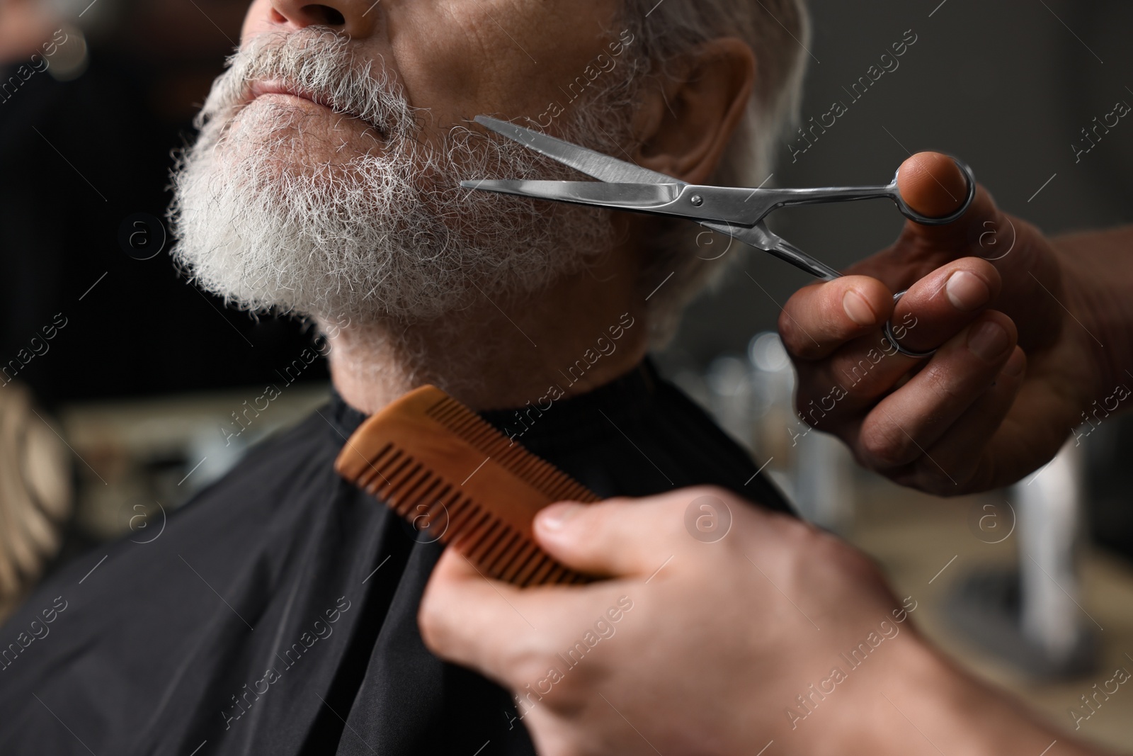 Photo of Professional barber trimming client's beard with scissors in barbershop, closeup