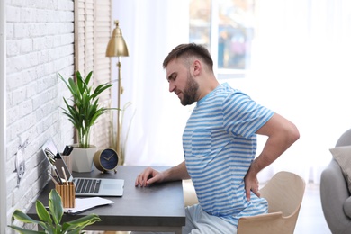 Photo of Young man suffering from back pain in office