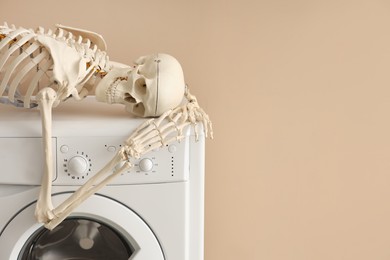 Photo of Waiting concept. Human skeleton lying on washing machine near beige wall indoors, space for text