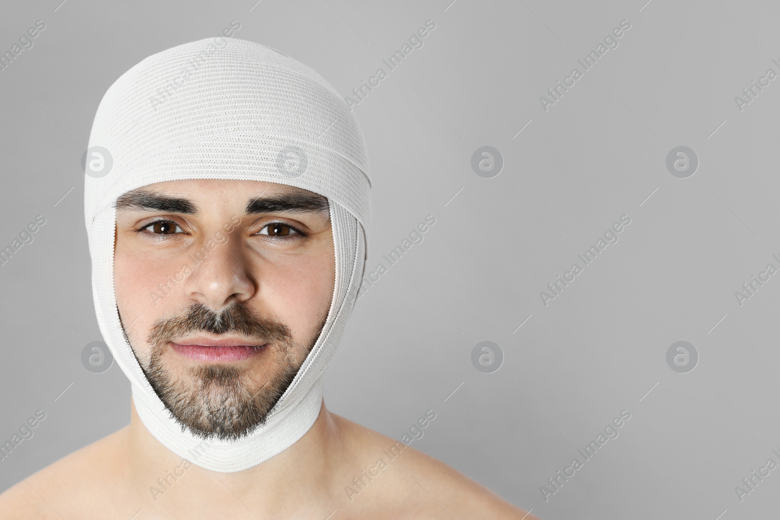 Photo of Bandaged young man after plastic surgery operation on grey background. Space for text