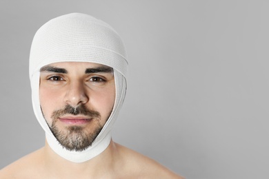 Photo of Bandaged young man after plastic surgery operation on grey background. Space for text