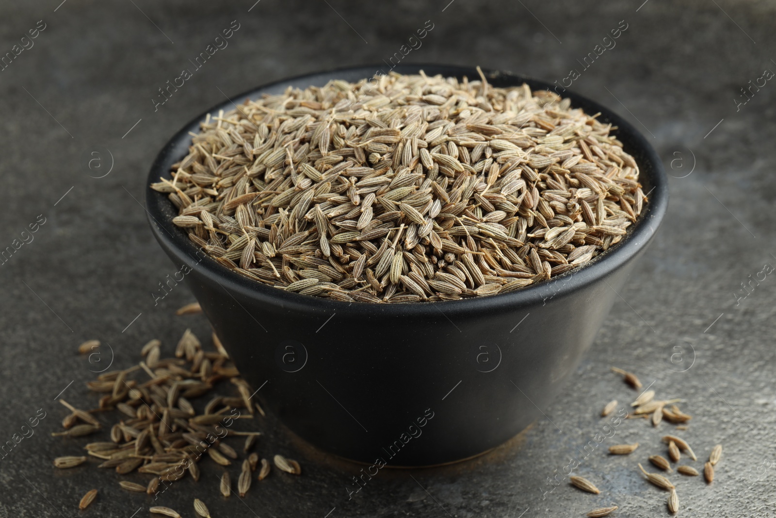 Photo of Bowl of caraway seeds on grey table, closeup