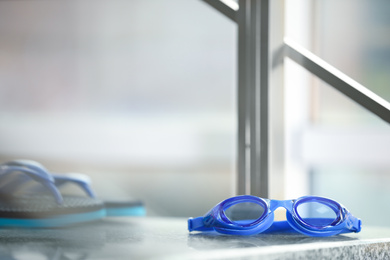 Photo of Blue swimming goggles and flip flops against blurred background. Space for text