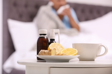 Photo of Cough syrups, lemon and cup of tea on table in bedroom