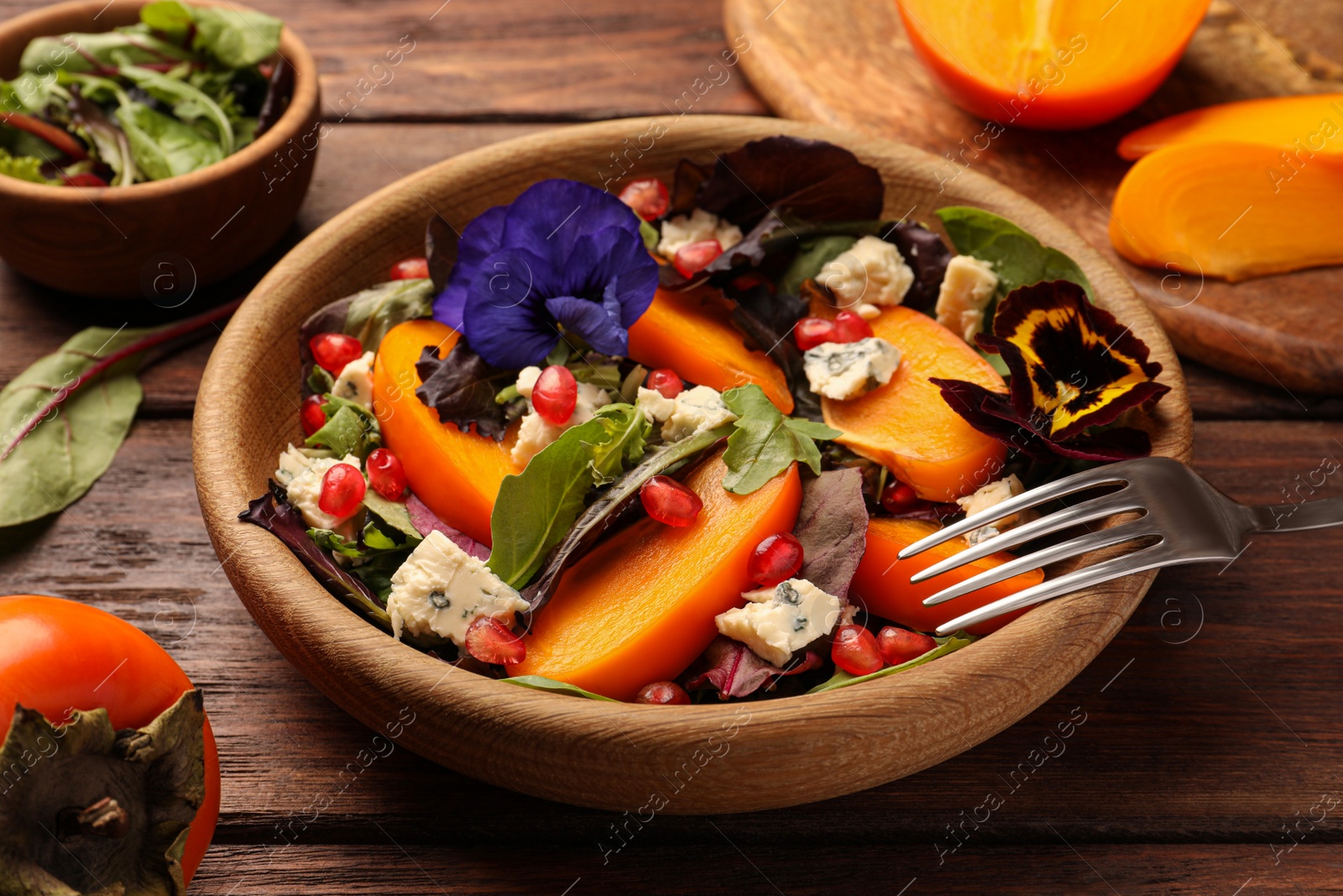 Photo of Delicious persimmon salad with cheese and pomegranate served on wooden table