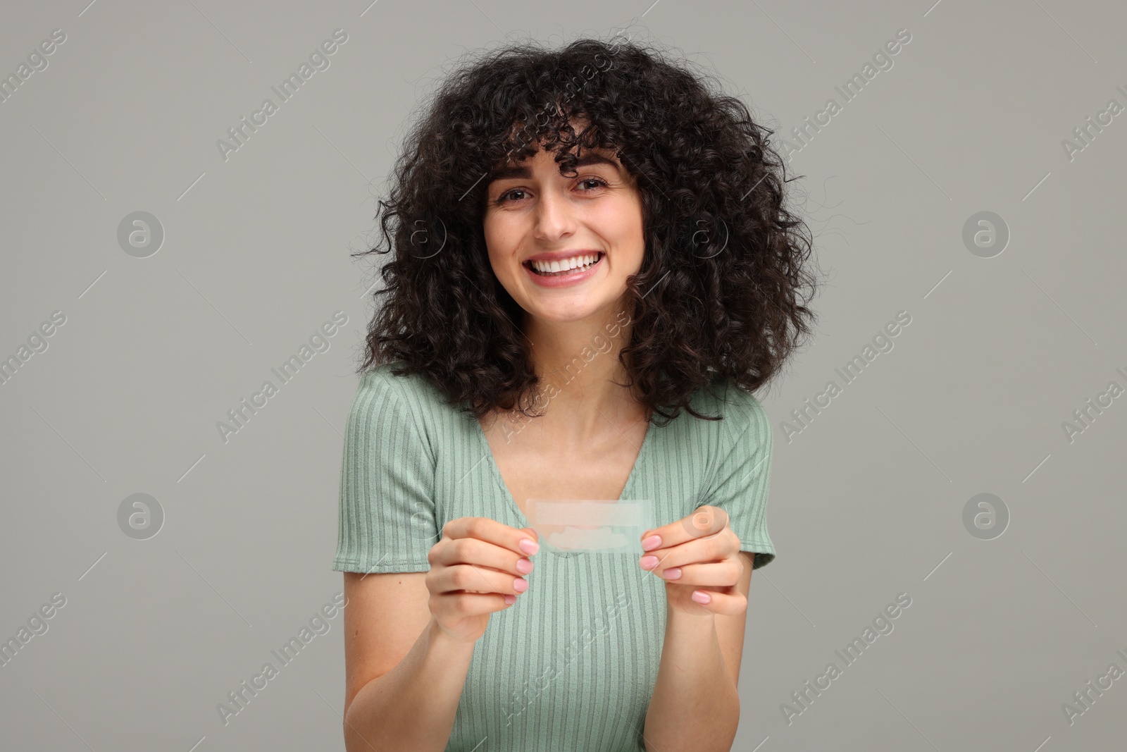 Photo of Young woman holding teeth whitening strips on grey background