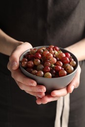 Woman holding bowl full of ripe gooseberries, closeup