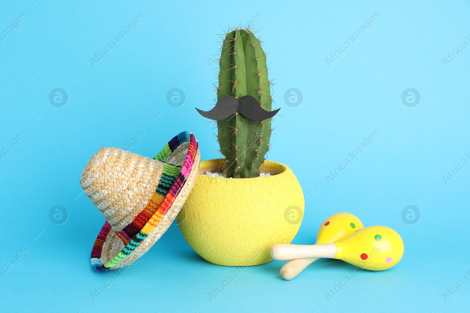 Photo of Mexican sombrero hat, cactus with fake mustache and maracas on light blue background