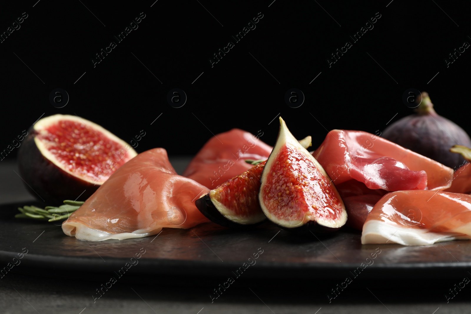 Photo of Delicious ripe figs and prosciutto served on table against black background