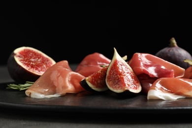 Delicious ripe figs and prosciutto served on table against black background