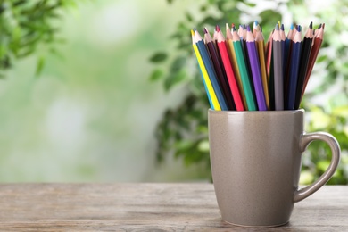 Photo of Colorful pencils in cup on wooden table against blurred background. Space for text