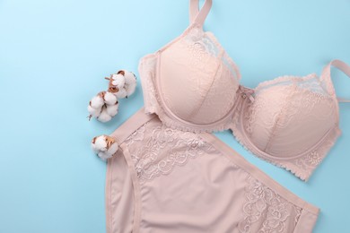 Photo of Elegant beige plus size women's underwear and fluffy cotton flowers on light blue background, flat lay