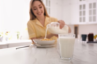 Woman with gallon bottle and breakfast cereal at white marble table in kitchen, focus on glass of milk